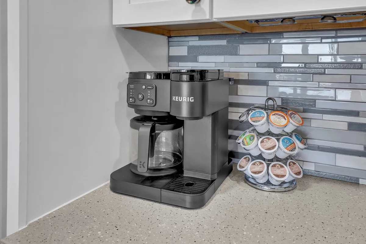 A Keurig coffee maker and pod holder rest on the kitchen counter, ready for morning rituals. The setup hints at cozy, social mornings with the backdrop of a well-equipped kitchen.