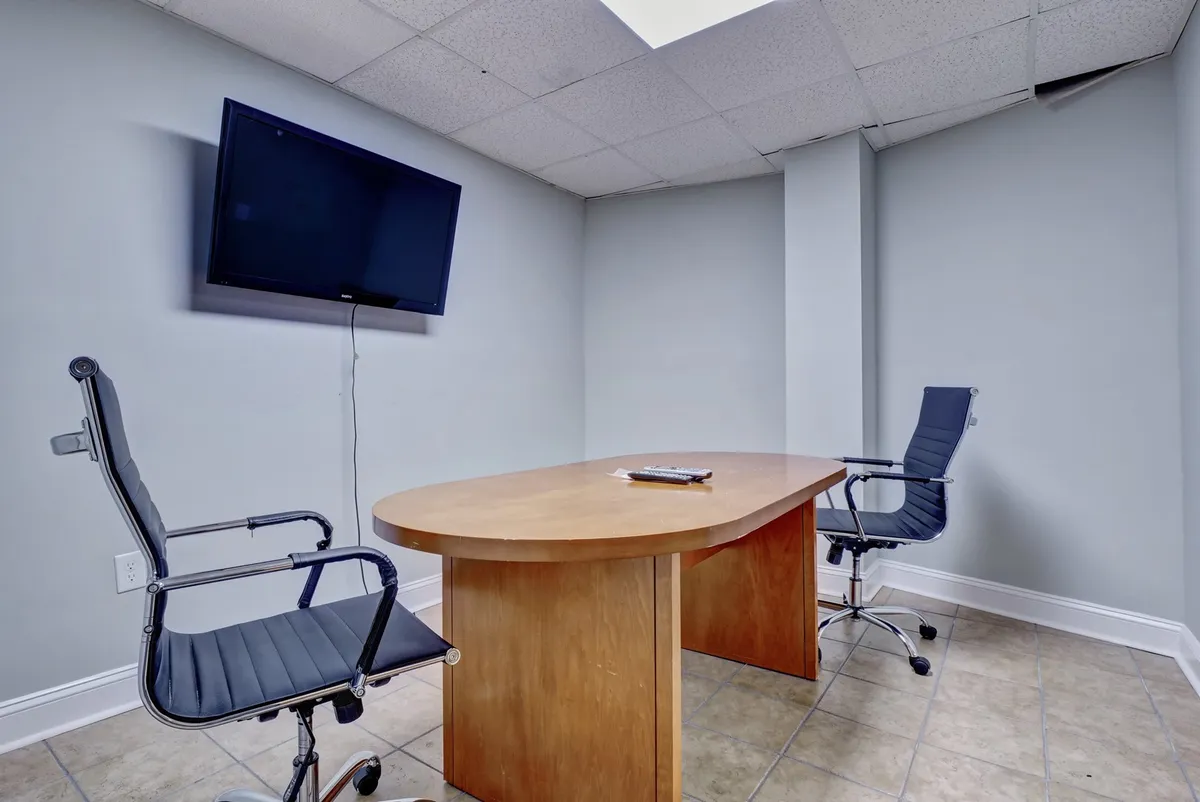 A modern conference or business space with a wooden table, two office chairs, and a wall-mounted television, this image conveys a formal yet inviting spot for meetings, brainstorming sessions, or remote work.