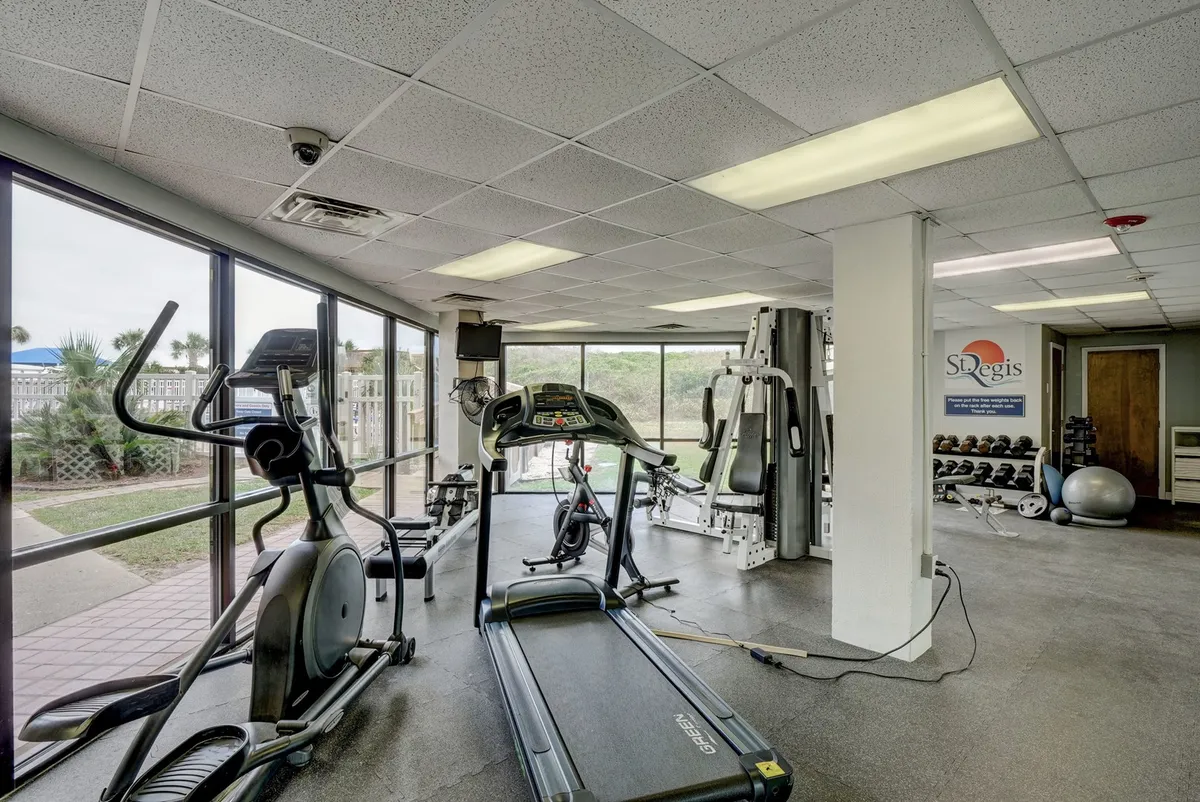 This interior image showcases the fitness center, featuring a treadmill, elliptical, weightlifting equipment, and large windows letting in abundant natural light. The scene conveys a modern, well-equipped gym space ideal for wellness breaks and maintaining health routines on the go.