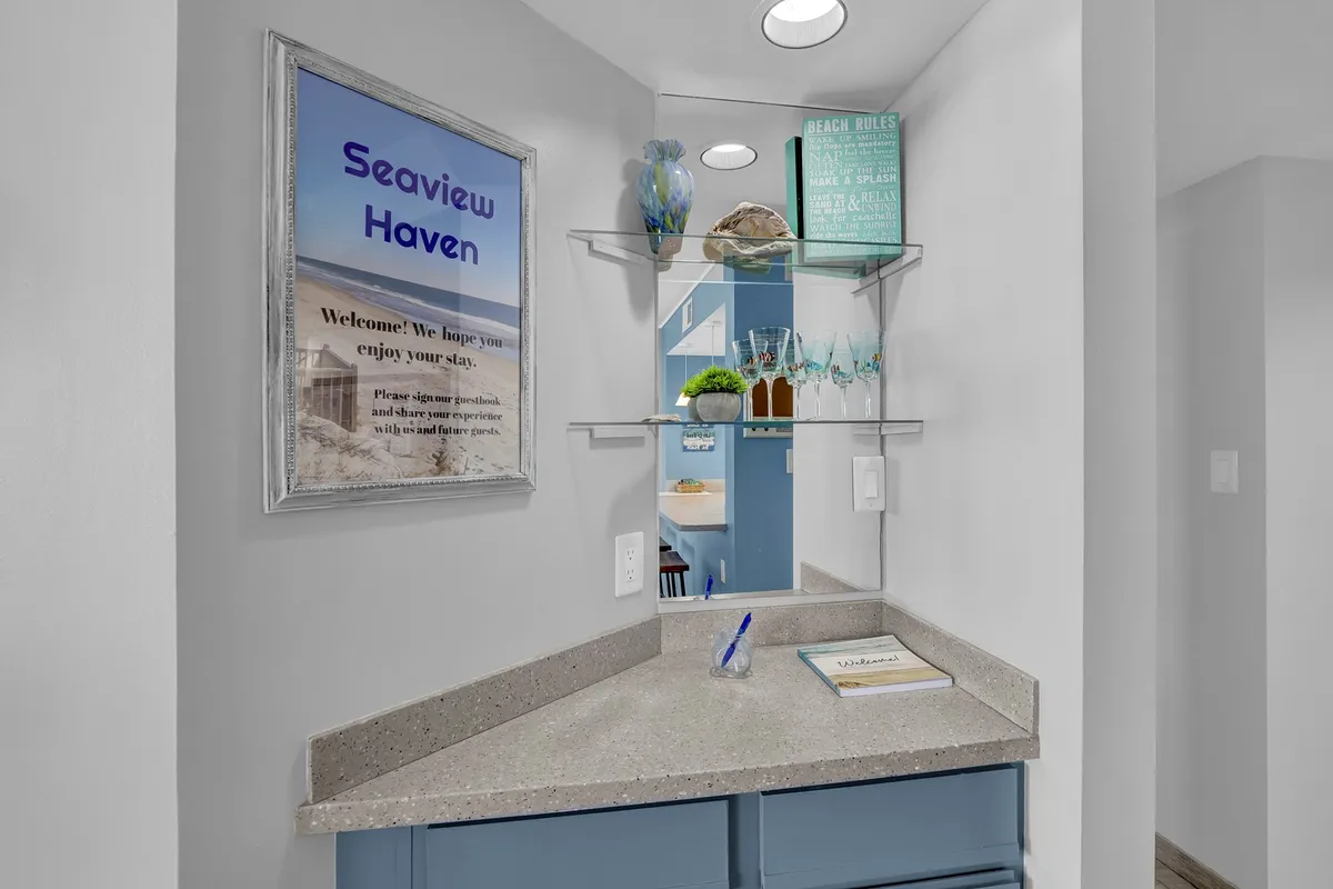A friendly welcome area with the 'Seaview Haven' sign and beach-themed decor. Shelves with decorative items and glasses suggest a warm, inviting first impression.