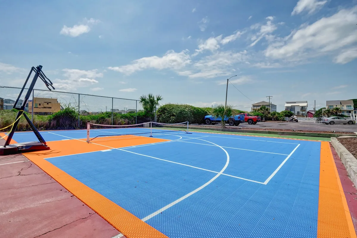 A vibrant, multi-colored basketball court with a prominent basketball hoop and tennis net. The area is designed for energetic outdoor play and community activities. The court exudes an energetic, playful vibe, inviting guests to enjoy basketball, tennis, or casual games with friends and family.