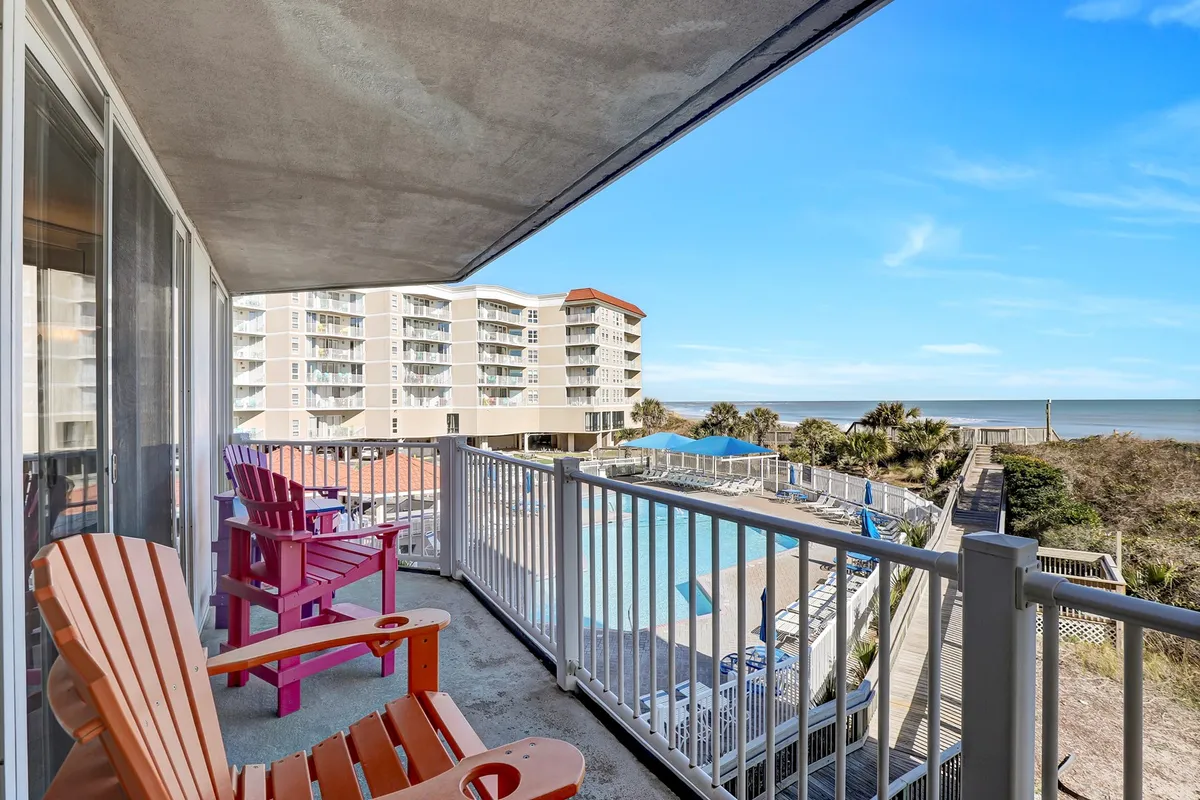A lively exterior shot featuring colorful Adirondack chairs arranged around the pool, with the condominium buildings and vast ocean view in the background. Families and friends enjoy relaxing by the poolside, soaking in the ocean breezes, and socializing under the open sky.