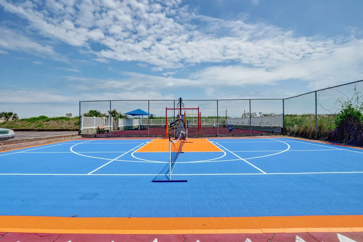 This exterior shot highlights a brightly colored court complete with a net and playground equipment in the background. The vibrant setting is designed for multiple sports such as basketball or tennis, and the surrounding area suggests community recreation and playful energy.