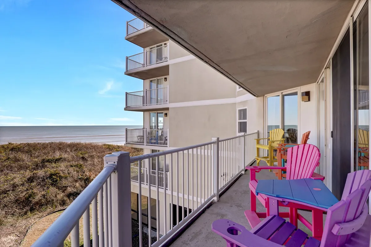 This exterior image displays colorful Adirondack chairs arranged on a spacious balcony or patio, facing out to a sweeping view of the ocean. The scene exudes a sense of relaxation and togetherness, suggesting a perfect spot for unwinding with friends or family while enjoying the beauty of the shoreline and sky.