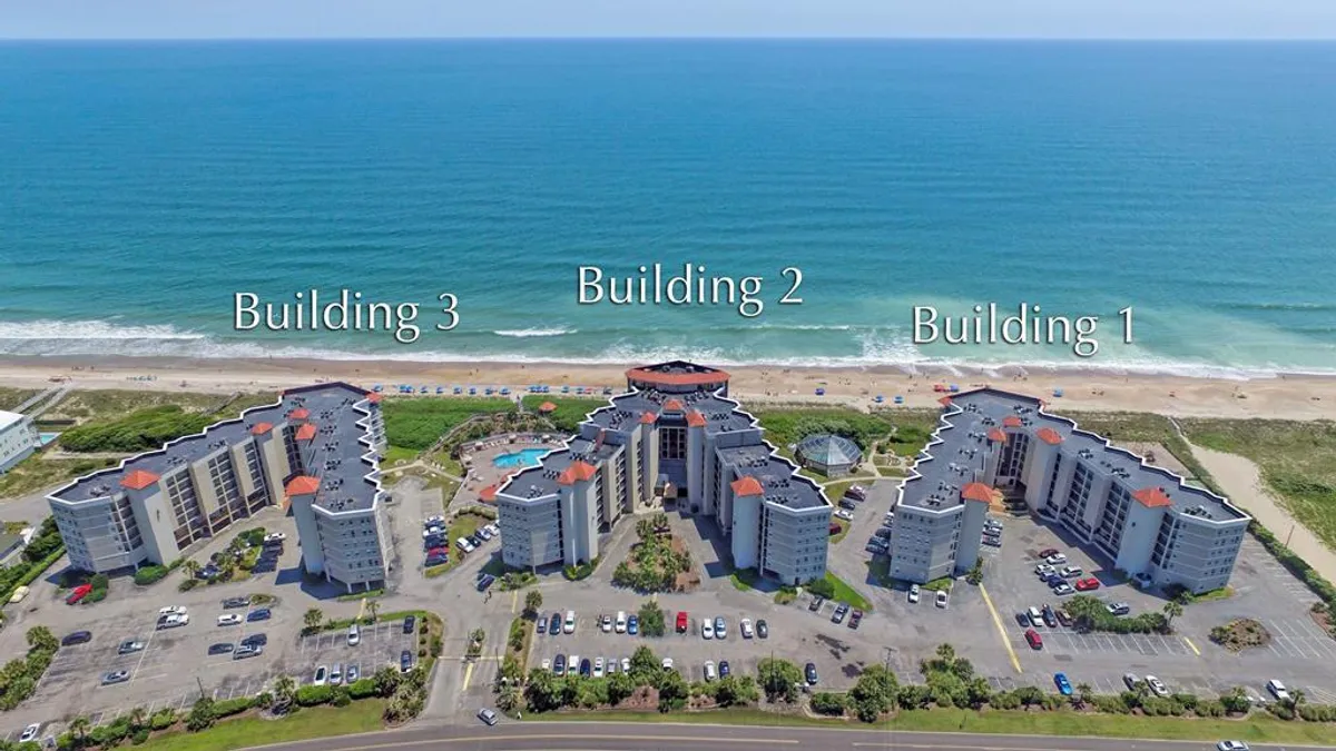 This exterior image captures three distinct buildings of the St. Regis property, with a sparkling swimming pool and the ocean visible in the background. The environment is inviting and relaxed, with spaces for sunbathing, swimming, and easy access to beach walks, suggesting both leisure and rejuvenation.