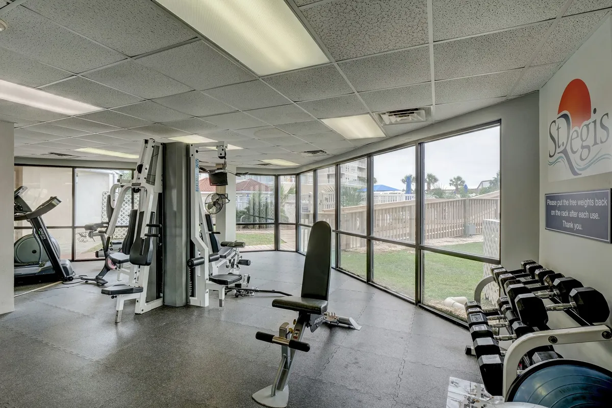 A bright, modern fitness center with large windows offering abundant natural light. Various exercise equipment, including treadmills and weight machines, is available, and the motivational branding on the wall sets an energetic tone. The clean, open layout encourages both solo workouts and group exercise.